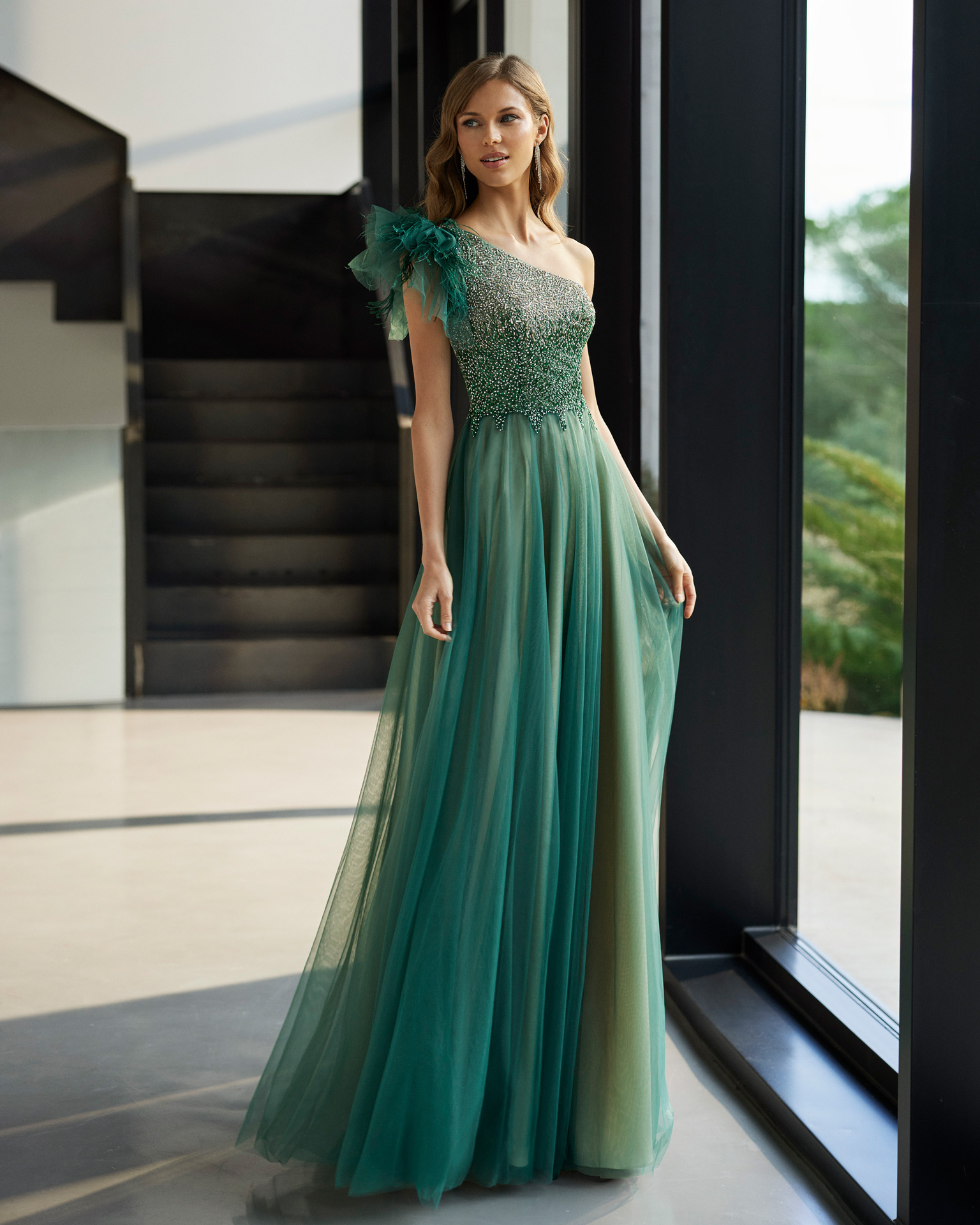 Fairytale style long cocktail dress. Made of tulle embellished with beadwork. With asymmetrical neckline and feathers. Marfil Barcelona look for parties and celebrations. MARFIL_BARCELONA.