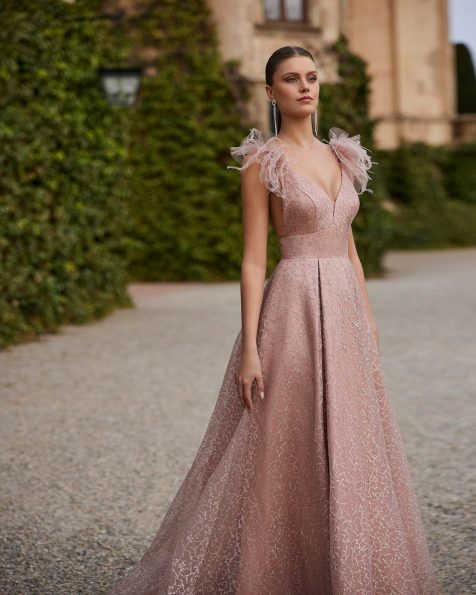 Long evening dress crafted in organza with glitter. Featuring a V-neckline, open back and straps with feathers. A Marfil Barcelona look. MARFIL_BARCELONA.