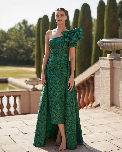 Long evening dress crafted in brocade. Featuring a bateau neckline, back zip, lace sleeve with feathers, and a decorative bow at the waist. A Marfil Barcelona look. MARFIL_BARCELONA.