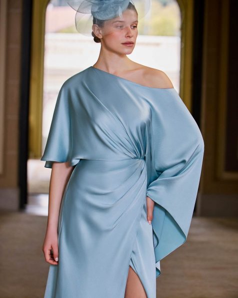 Vestido de fiesta largo, confeccionado en raso texturizado. Con escote asimétrico, manga capa y falda con abertura lateral. MARFIL_BARCELONA.