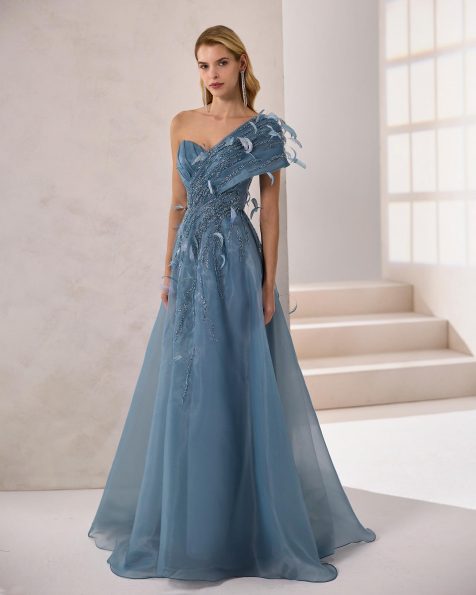 Vestido de fiesta largo. Confeccionado en organza. Escote asimétrico y cuerpo con pedrería. Detalles de plumas. Incluye chal. MARFIL_BARCELONA.